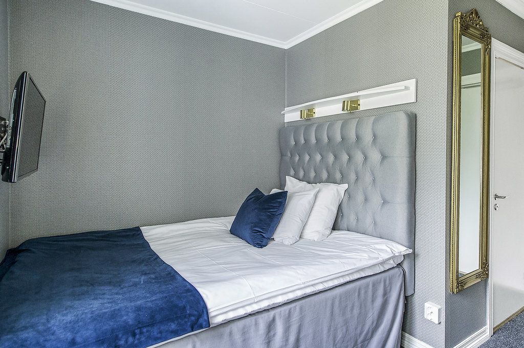 Ein ordentlich bezogenes Bett mit grauem Kopfteil, weißer Bettwäsche und einem blauem Kissen.