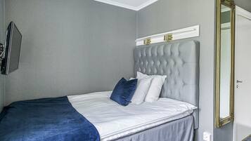Una cama bien hecha con cabecera gris, ropa de cama blanca y almohada decorativa azul.