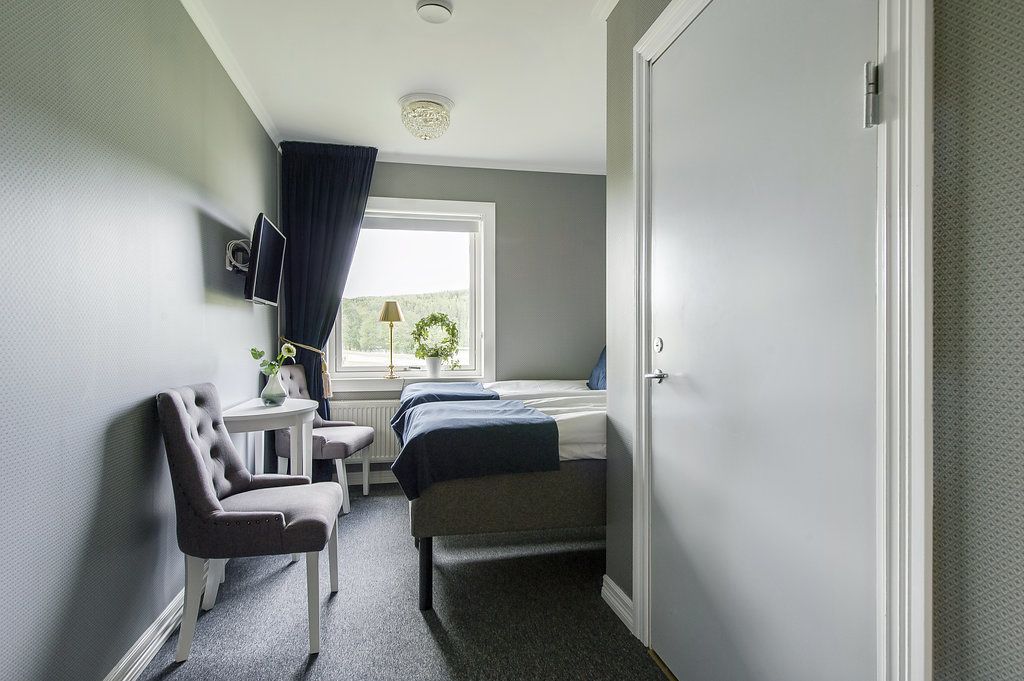 Habitación de hotel compacta con cama, escritorio, silla, televisión y ventana con cortinas.