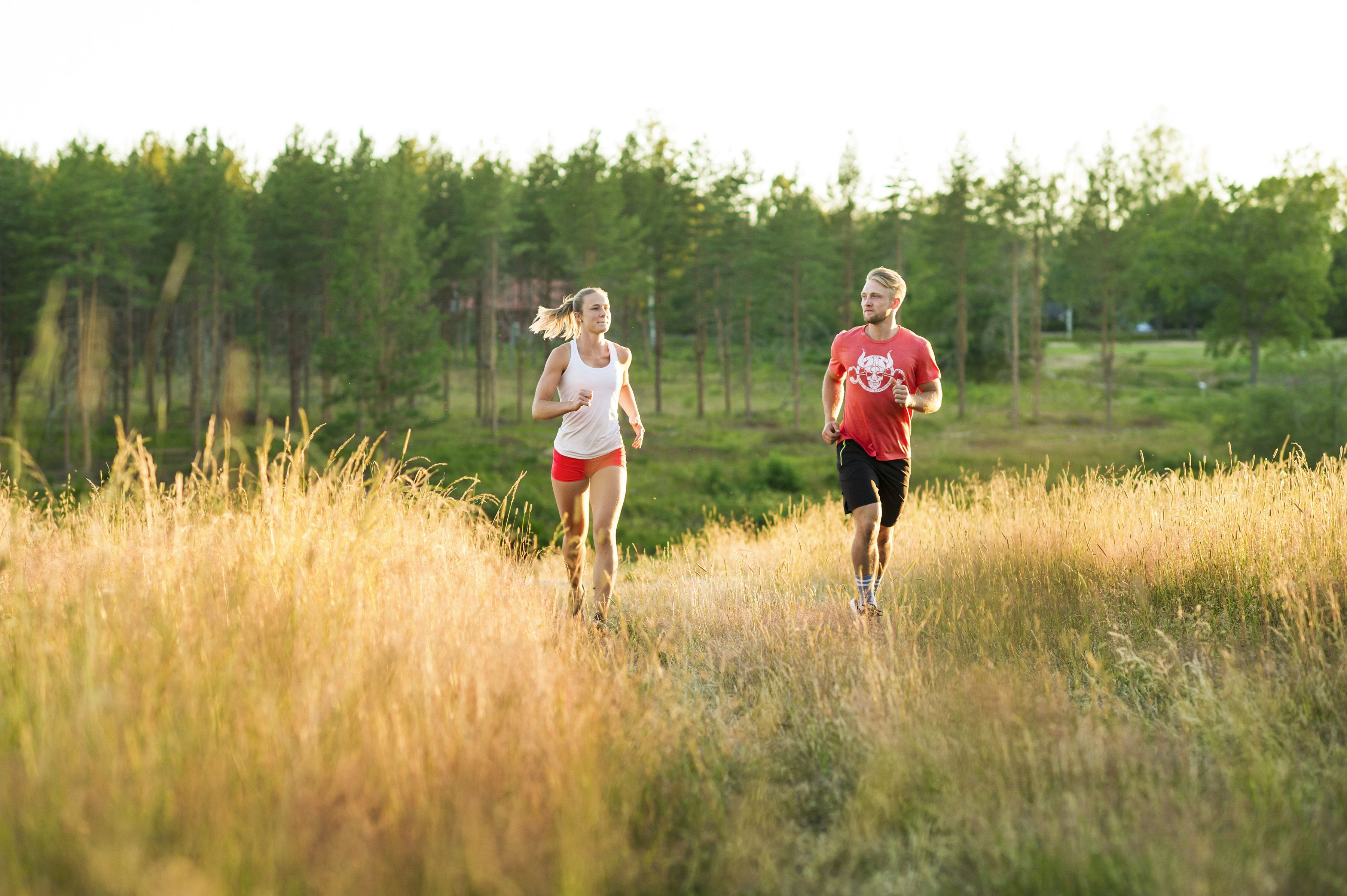Two people jogging in a grassy field with trees in the background.