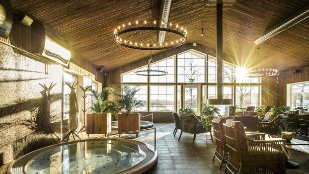 A spacious indoor area with a hot tub, wicker furniture, and large windows allowing natural light.
