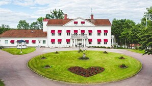 A large white building with red shutters, a central entrance, and a heart-shaped flower bed in the front.