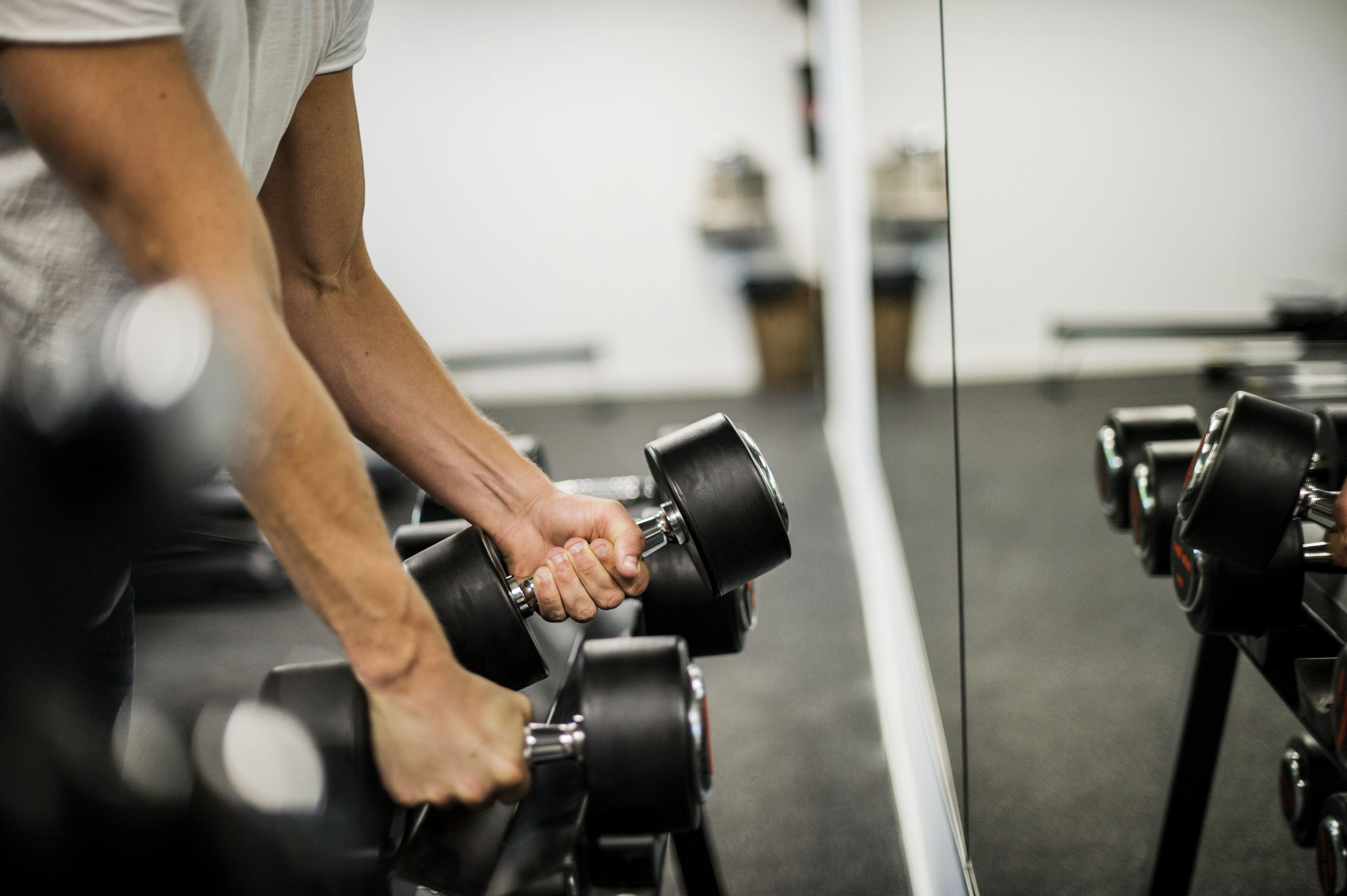 Ett gym med flera rader av hantlar och en spegel som reflekterar träningsutrustningen.
