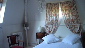 A bedroom with a bed, a chair, a nightstand, a lamp, and a radiator. - Villa des Iris (Saint-Felix)