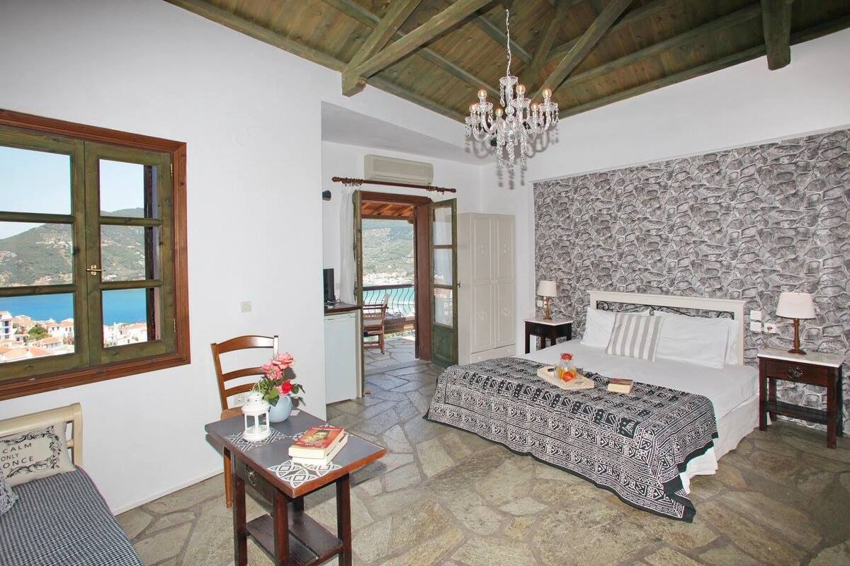 Un dormitorio con cama, una mesa con un florero, una araña y vista al mar.