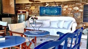 A cozy seating area with a white sofa, blue chairs, and round tables. - Aperanto Galazio (Skopelos)