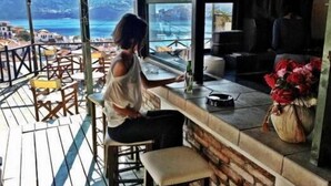 A person seated at a bar with a view of a coastal town. - Aperanto Galazio (Skopelos)