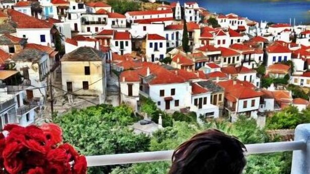 A balcony with a table, a vase of red flowers, and a glass of drink. - Aperanto Galazio (Skopelos)