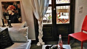 A cozy living room with a white sofa, a red chair, a painting on the wall, and a view of buildings through a large window. - Aperanto Galazio (Skopelos)