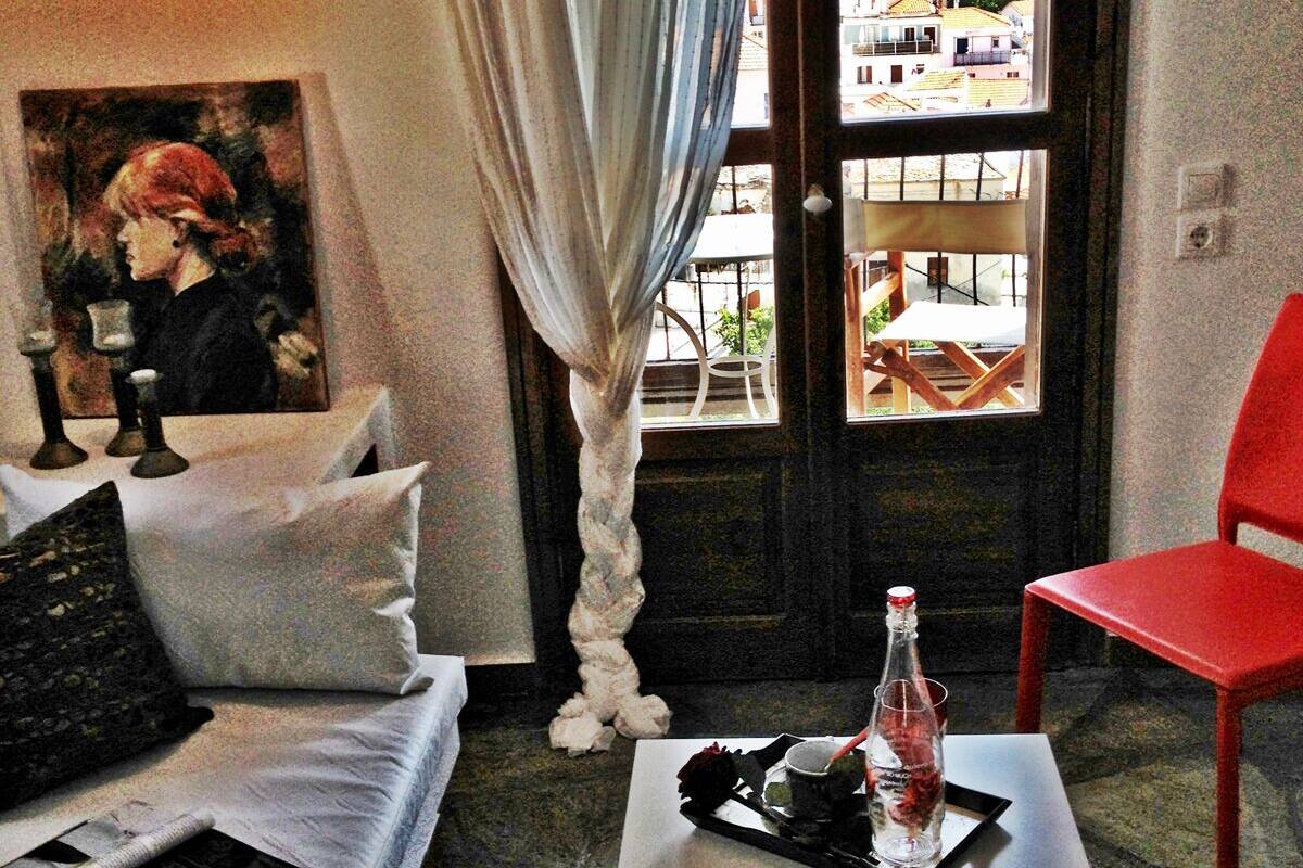 Una sala de estar acogedora con un sofá blanco, un sillón rojo, un cuadro en la pared y vistas a edificios a través de un ventanal grande.