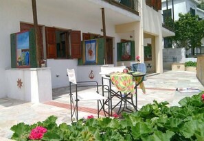 A covered outdoor seating area with a table and chairs, surrounded by potted plants and a tiled floor. - Aperanto Galazio (Skopelos)
