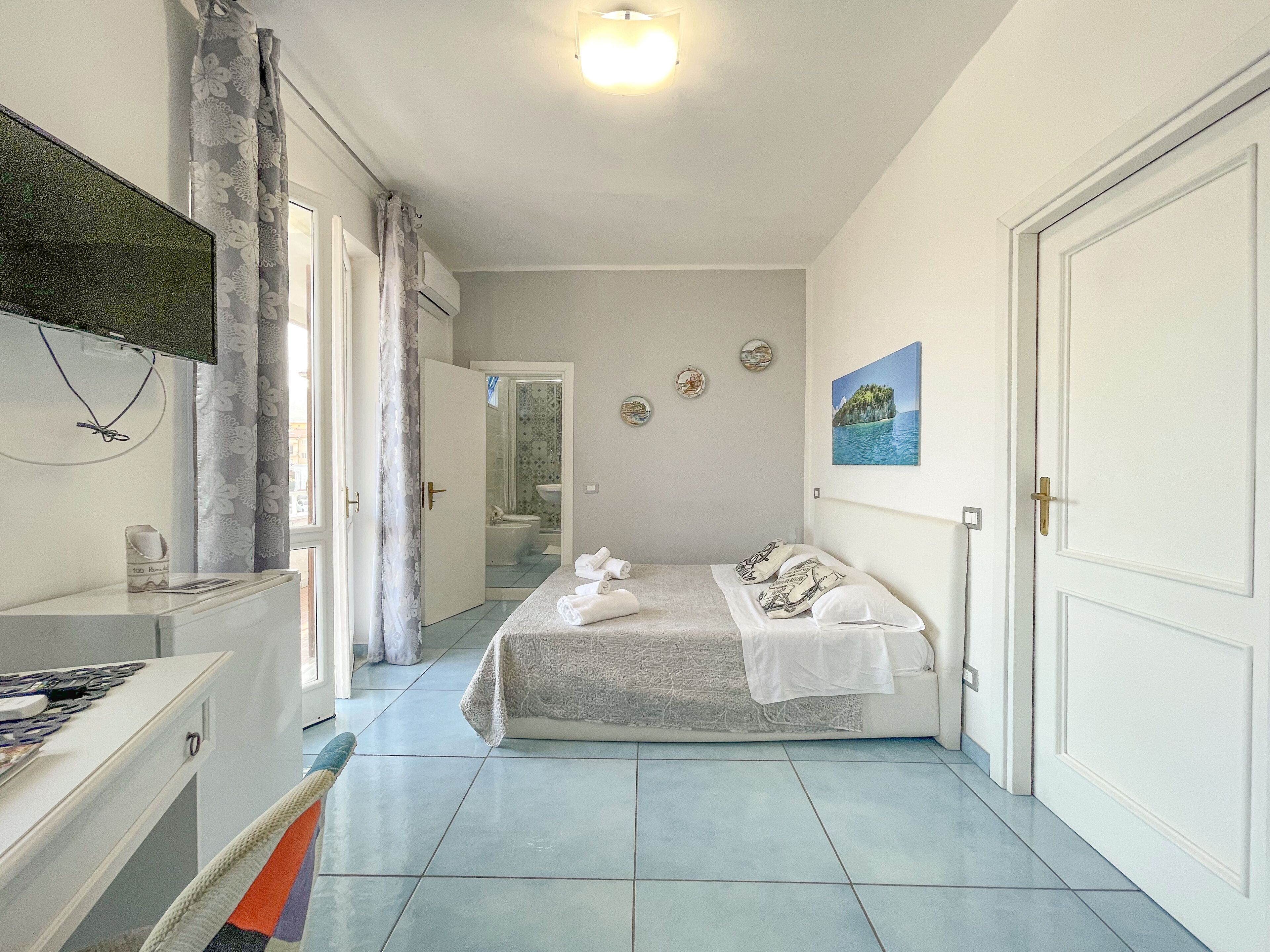 A bedroom with a bed, a desk, and a bathroom visible through an open door.