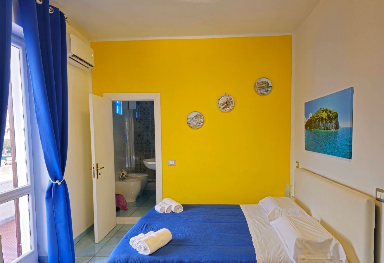 A room with a bed, a bathroom visible through an open door, and a wall with decorative plates and a painting.