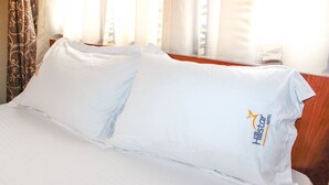 Ein ordentlich bezogenes Bett mit weißen Leinen und einem Kopfkissen mit dem Logo des Hillstar Hotels.