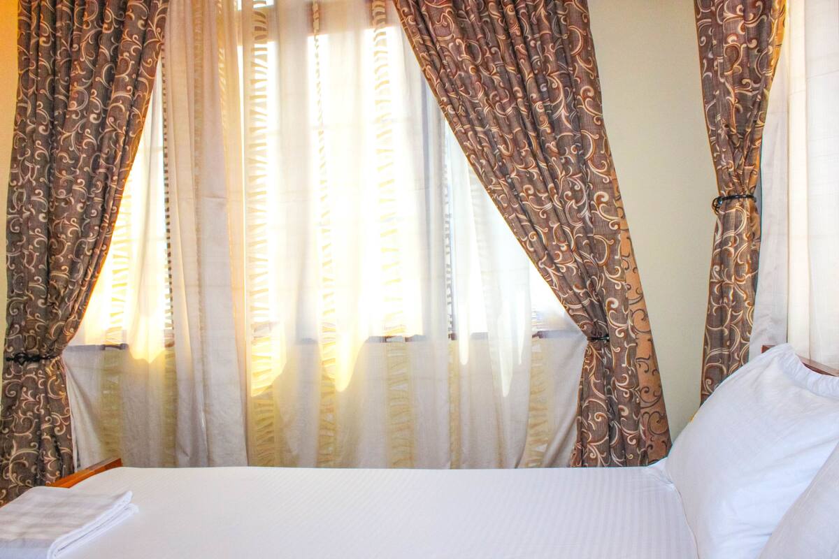 Ein Hotelzimmer mit Bett, Vorhängen und einem Fenster.