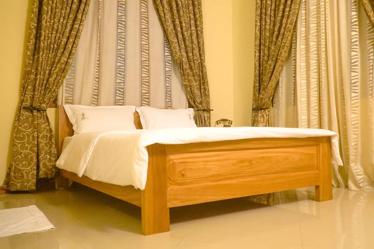 Ein hölzernes Bett in einem Zimmer mit gemusterten Vorhängen und einer weißen Bettdecke.