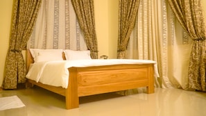 Una cama de madera en una habitación con cortinas estampadas y una colcha blanca.