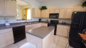 A kitchen with light-colored cabinets, a central island, a black refrigerator, a microwave, a stove, and a dishwasher. - Ly53792 - Emerald Island - 6 Bed 5 Baths Villa (Kissimmee)