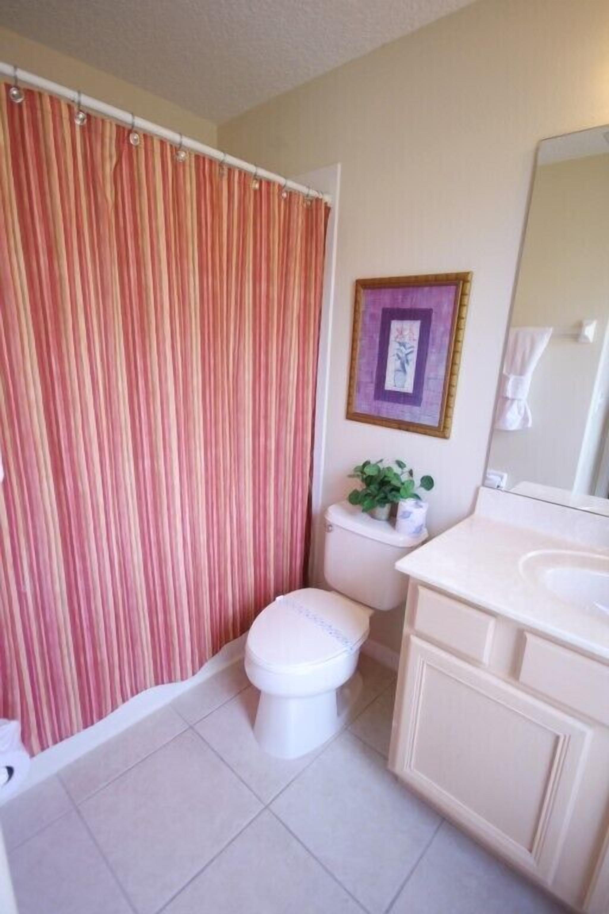 A bathroom with a shower curtain, toilet, sink, and a framed picture on the wall.