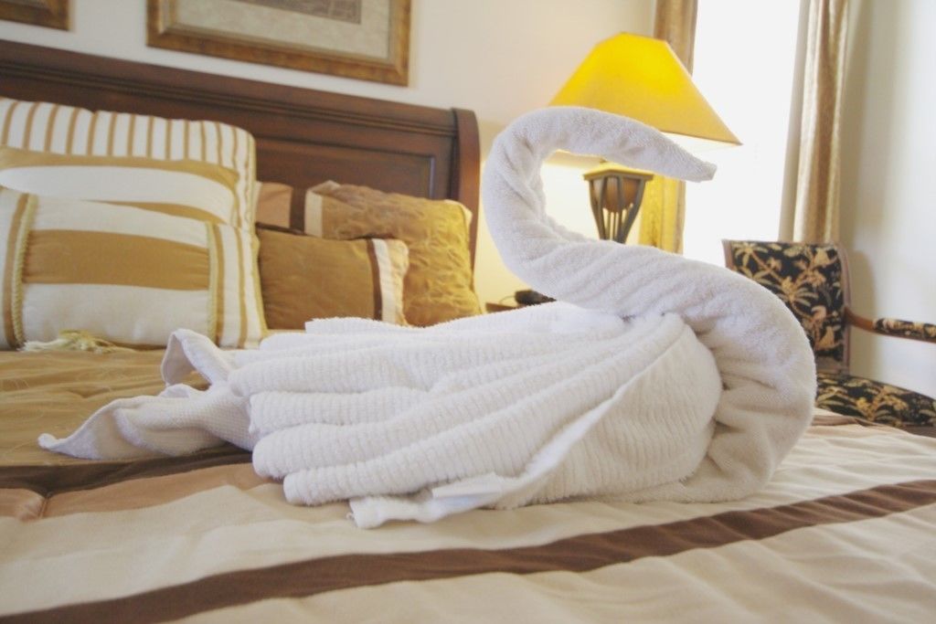 Ein Bett mit einem weißen, zu einem Schwan geformten Handtuch, einem hölzernen Kopfteil und einer gelben Lampe.