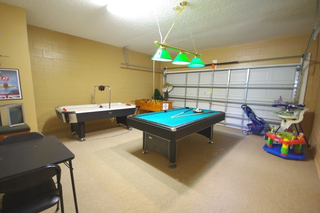 A room with a pool table, a billiards table, a small table with toys, and a garage door in the background.