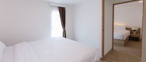 Una habitación de hotel moderna con una cama grande, suelo de madera y vistas a otra habitación por una puerta abierta.