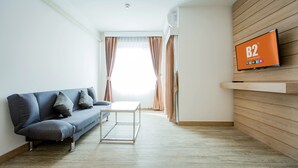 Un salon moderne avec un canapé gris, une petite table blanche et un téléviseur fixé au mur, qui est en bois.