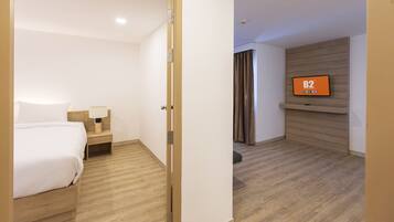 A hotel room with a bed, nightstand, lamp, and a TV mounted on the wall.
