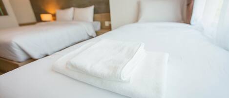 A hotel room with two beds, one larger and one smaller, and a neatly folded white towel on the larger bed.