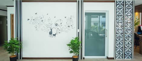 A room with a large decorative wall featuring a tree and deer, a sliding glass door, and a patterned partition.