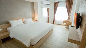 Une chambre d’hôtel avec un grand lit, une tête de lit en bois, une table de chevet avec une lampe, un téléviseur fixé au mur et une fenêtre avec des rideaux.