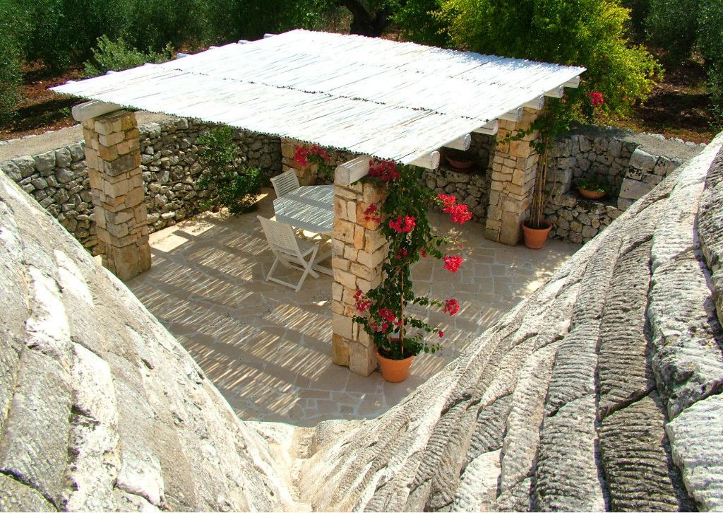 A stone patio with a metal roof table, surrounded by stone walls and potted plants.