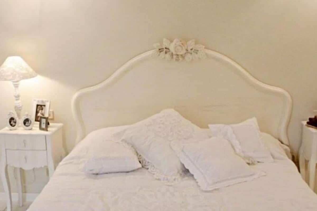Une chambre à coucher avec un lit blanc, deux tables de chevet, une lampe et une tête de lit décorative.