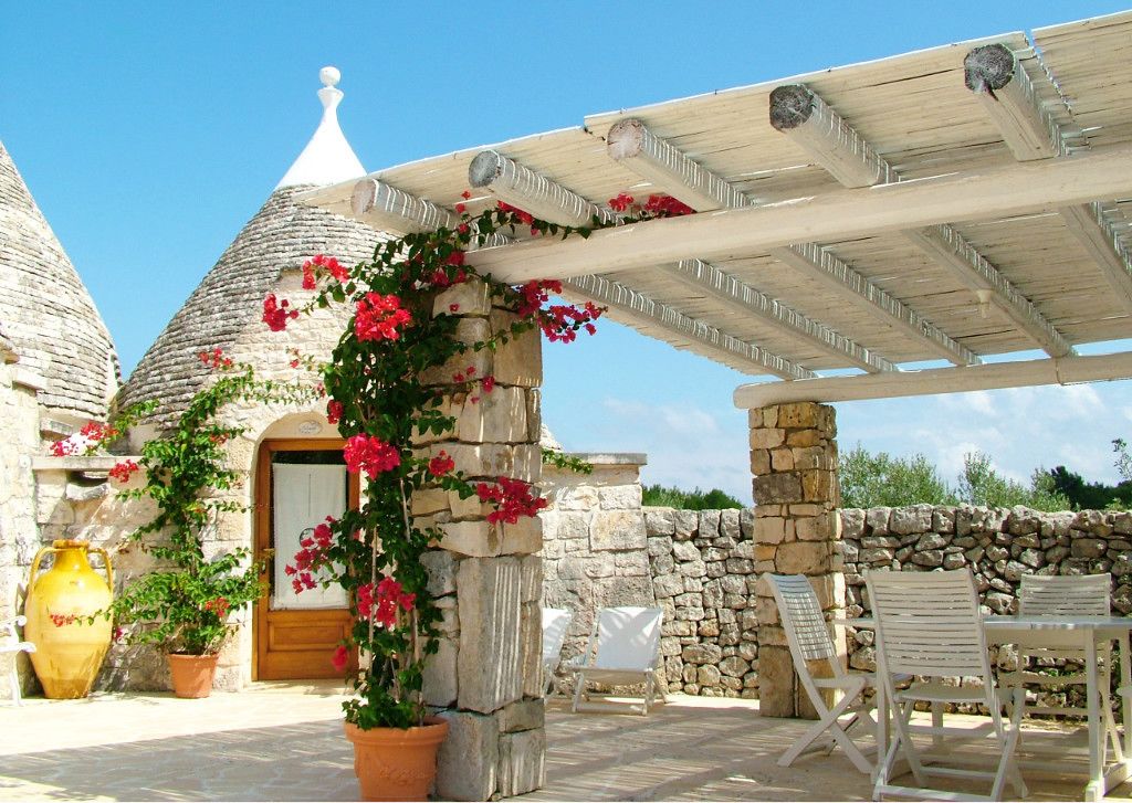 A stone building with a conical roof, a wooden pergola, and outdoor seating.