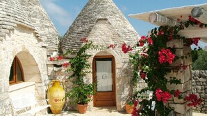 A stone building with a wooden door and a large yellow vase. - Masseria Cappuccini (Ostuni)