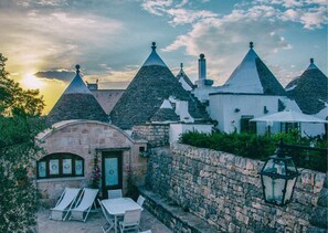 A traditional stone building with conical roofs, a stone wall, and a small patio with chairs and a table. - Masseria Cappuccini (Ostuni)