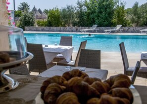 A poolside dining area with wicker chairs and a table set for two, overlooking a clear blue pool. - Masseria Cappuccini (Ostuni)