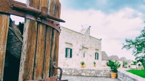 A rustic wooden barrel with metal bands, a stone pathway, and a building with green shutters in the background. - Masseria Cappuccini (Ostuni)