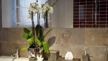 A bathroom with a sink, two orchid plants in glass containers, a mirror, and a tiled wall.