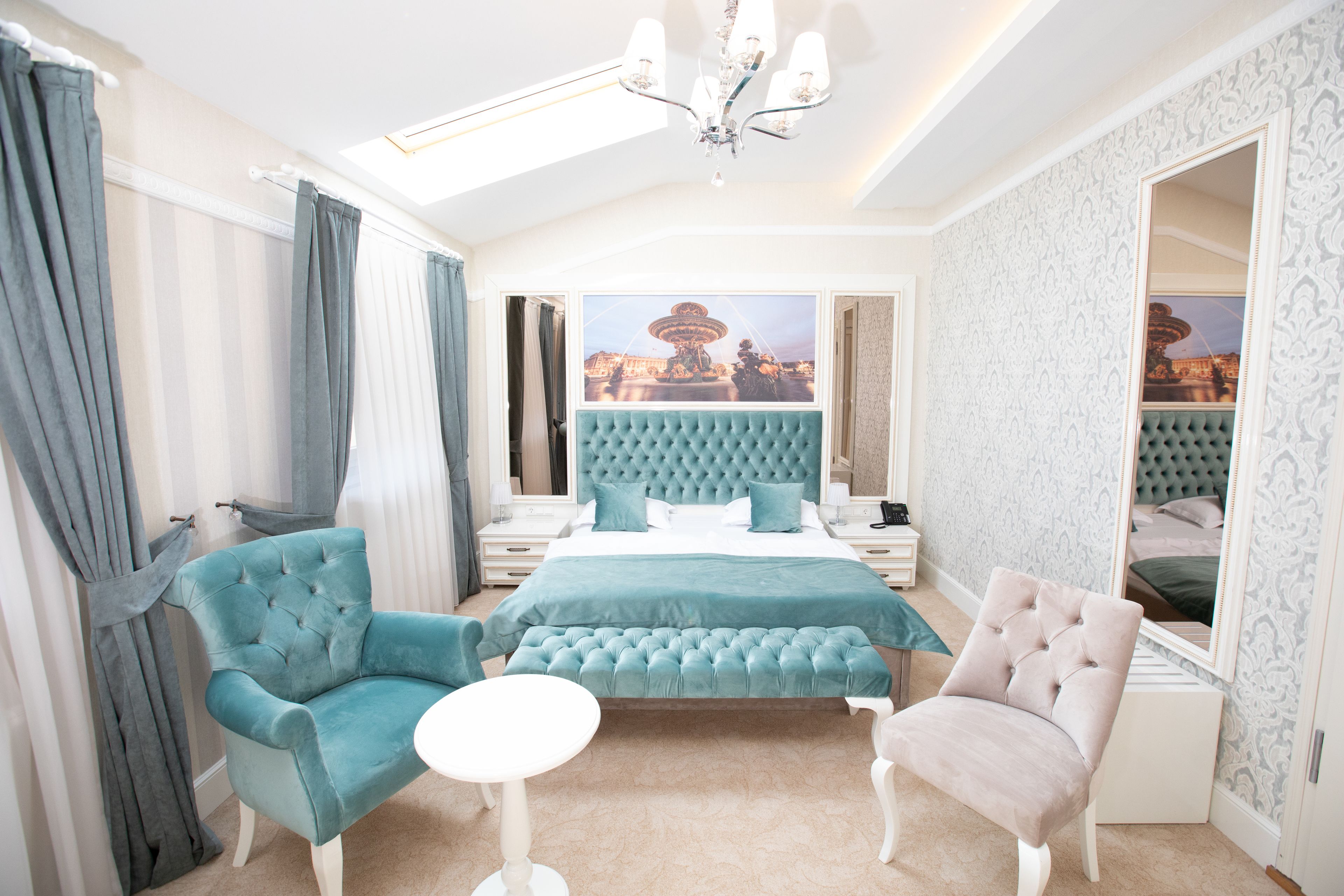 A bedroom with a large bed, two armchairs, a small table, and a large mirror.