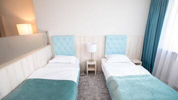 A hotel room with two single beds, a nightstand, a lamp, and a window with curtains.