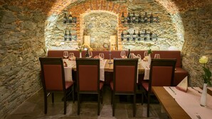 Un restaurant avec un mur en pierre servant de décor, des tables en bois et des sièges rembourrés de couleur rouge.