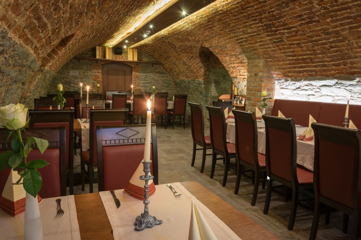 An interior with stone arches and tables set for dining, featuring candles and a vase with a flower.