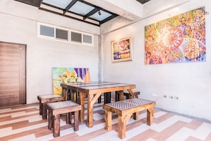 A spacious room with a large wooden dining table and benches, a ceiling with skylights, and two artworks on the walls. - Mabuli Inn (Magong)