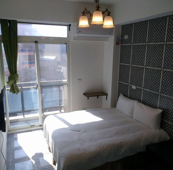 A hotel room with a bed, a window with curtains, a wall-mounted shelf, and a patterned wall.