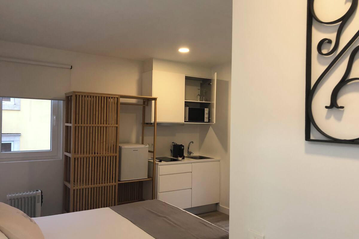 A compact bedroom with a bed, a wardrobe, a small kitchenette, and a window.