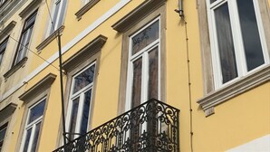 Een geel gebouw met veel ramen en een balkon met versierde metalen hekwerk.