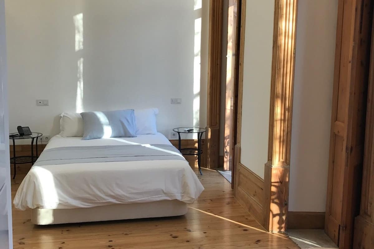 A bedroom with a large bed, wooden flooring, and a small table.