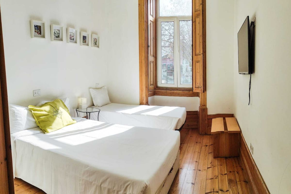 A bedroom with two beds, a window, a TV, and a wooden floor.