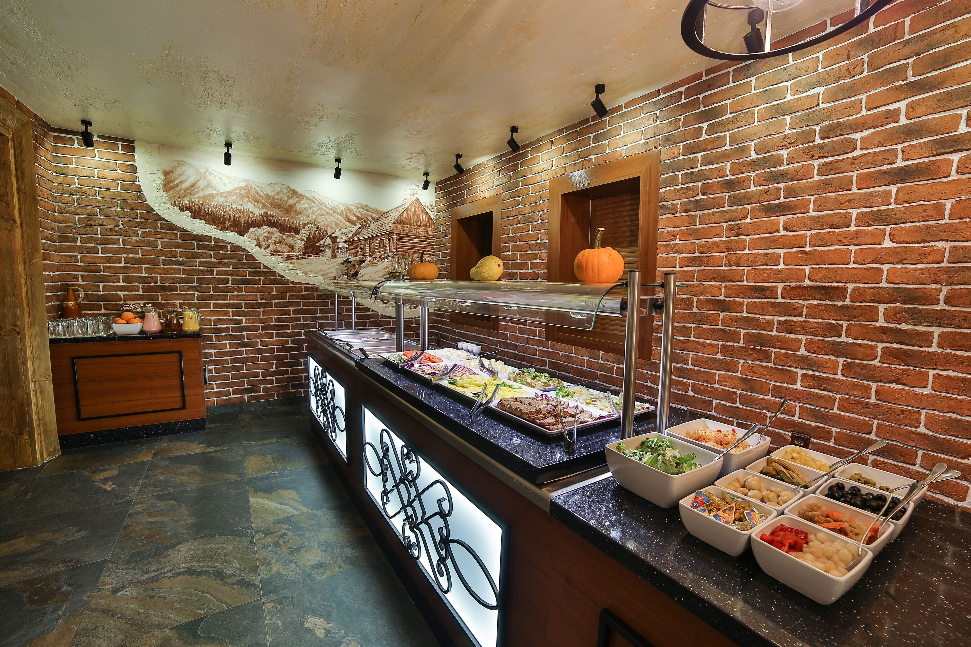 A buffet area with various food options, a brick wall, and a mural of a mountain scene.